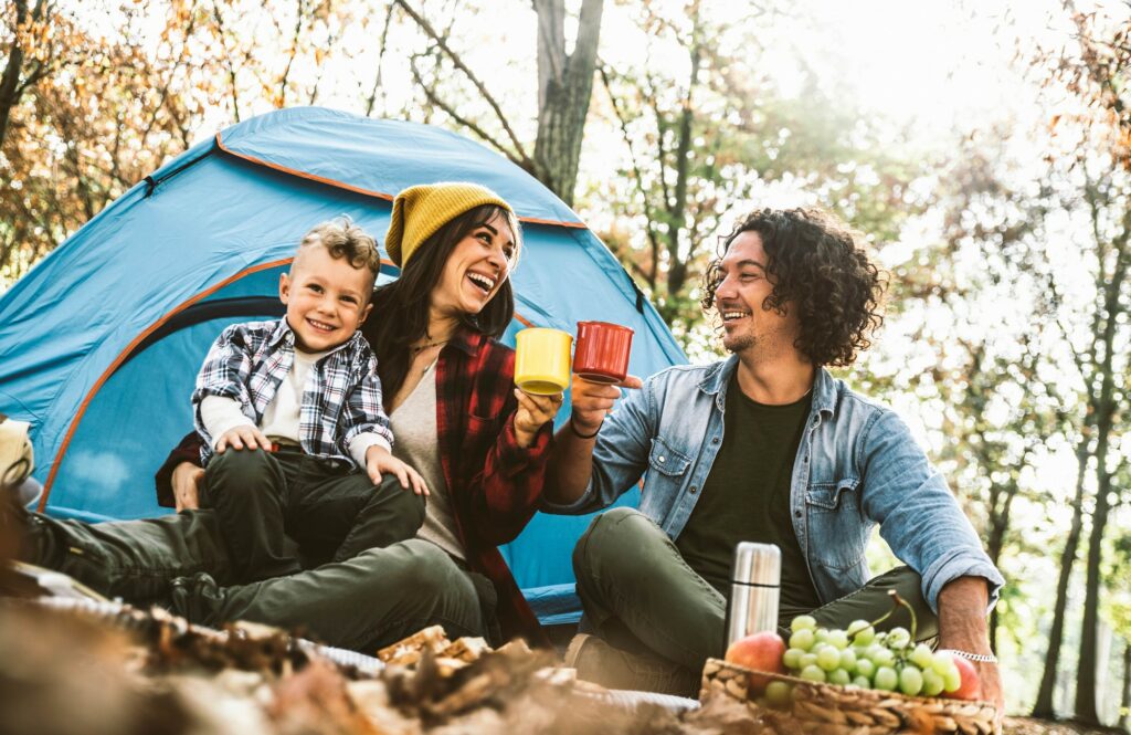 Happy family camping in the forest drinking tea sitting in touristic tent